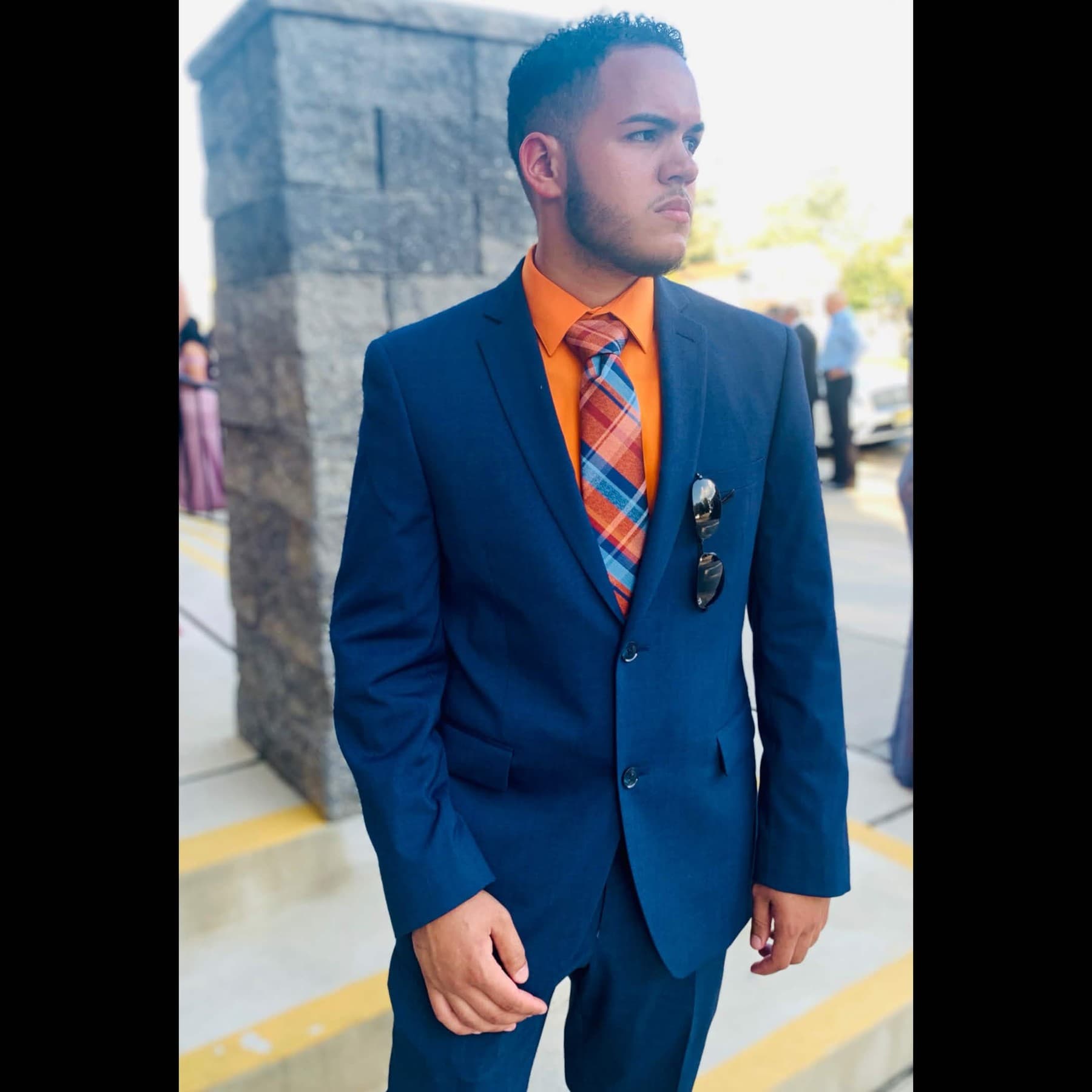 Raf (Rafmeta / @rafmeta) in a navy suit, orange shirt, and plaid tie